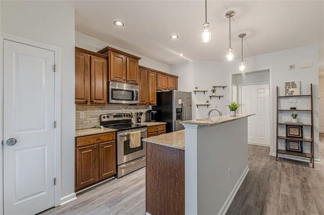 kitchen featuring pendant lighting, appliances with stainless steel finishes, light hardwood / wood-style floors, and an island with sink