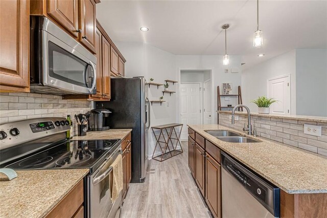 kitchen with stainless steel appliances, hanging light fixtures, sink, tasteful backsplash, and light wood-type flooring