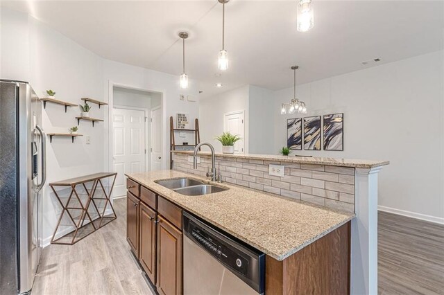 kitchen with tasteful backsplash, stainless steel appliances, hanging light fixtures, sink, and light hardwood / wood-style flooring