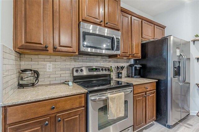 kitchen with light stone countertops, appliances with stainless steel finishes, decorative backsplash, and light hardwood / wood-style flooring