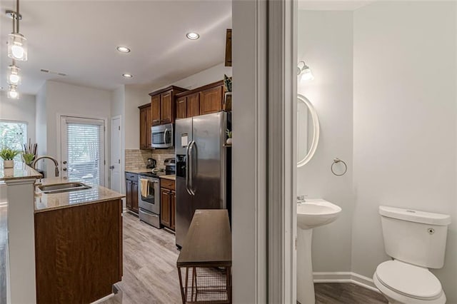 kitchen featuring tasteful backsplash, light stone counters, appliances with stainless steel finishes, sink, and light hardwood / wood-style floors