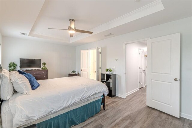 bedroom with wood-type flooring, ceiling fan, crown molding, and a tray ceiling