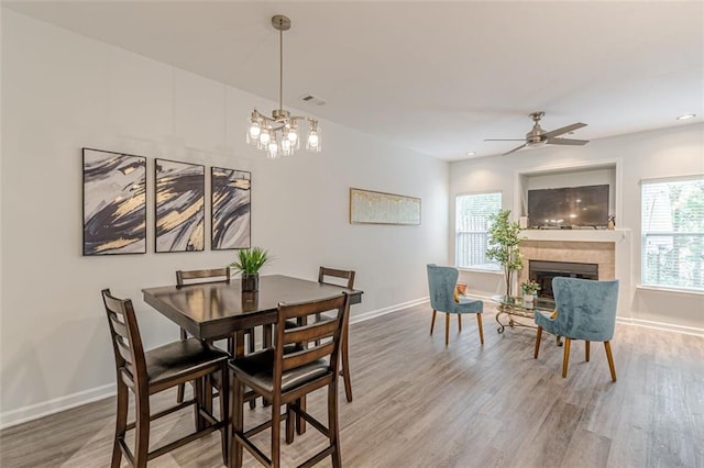 dining space featuring hardwood / wood-style floors, a tiled fireplace, and ceiling fan with notable chandelier