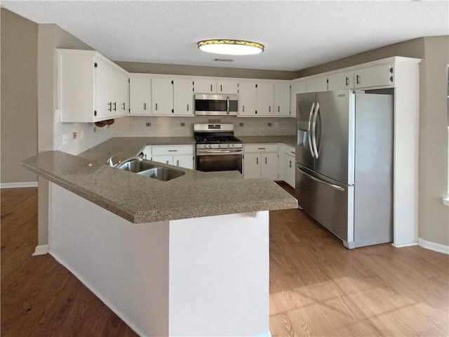 kitchen featuring light wood finished floors, a peninsula, stainless steel appliances, white cabinetry, and a sink