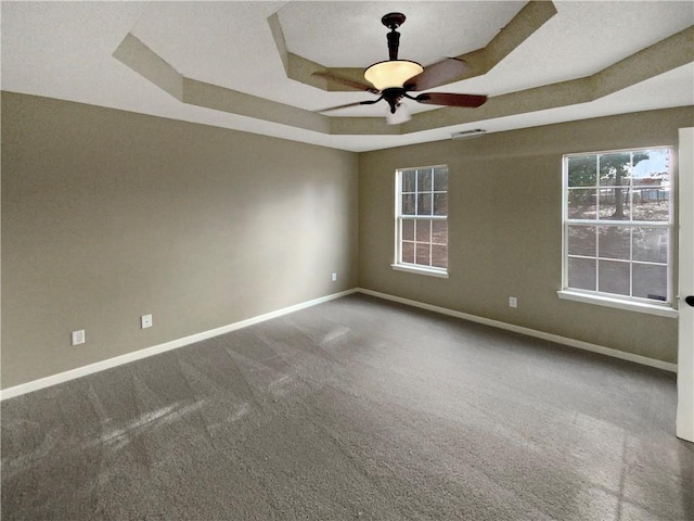 carpeted spare room featuring visible vents, a raised ceiling, baseboards, and a ceiling fan