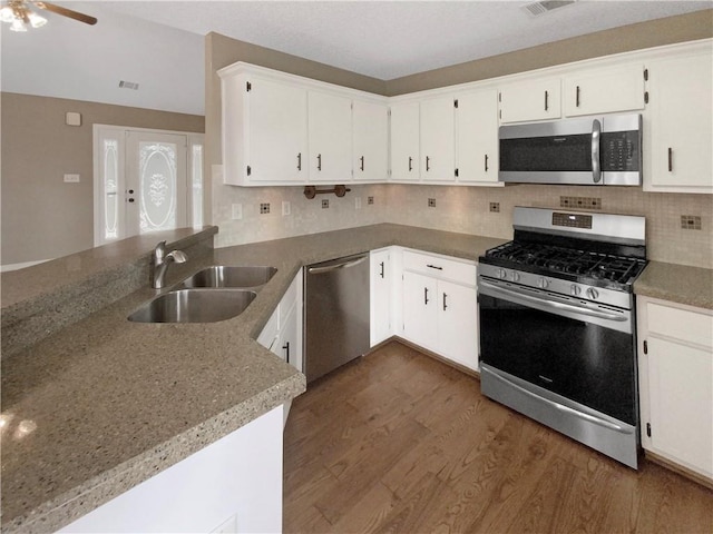 kitchen featuring dark wood finished floors, a peninsula, a sink, appliances with stainless steel finishes, and backsplash