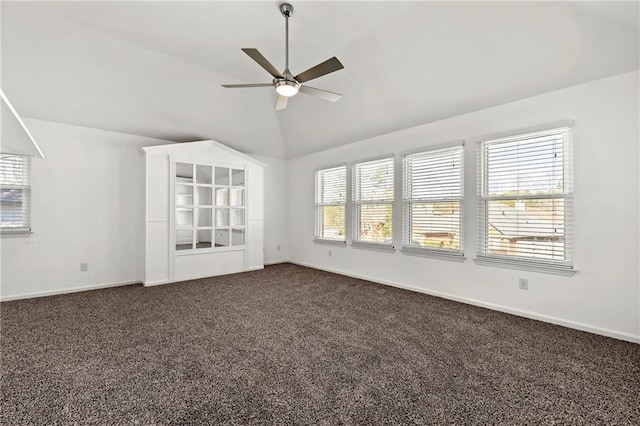 empty room with vaulted ceiling, dark colored carpet, a ceiling fan, and baseboards