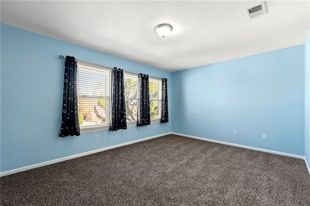 spare room featuring dark colored carpet, visible vents, and baseboards