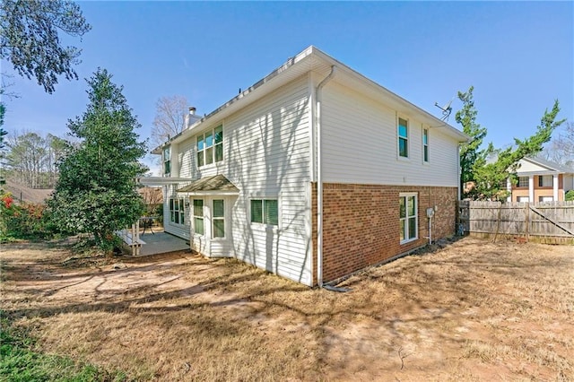 view of property exterior featuring a patio area, brick siding, fence, and a chimney