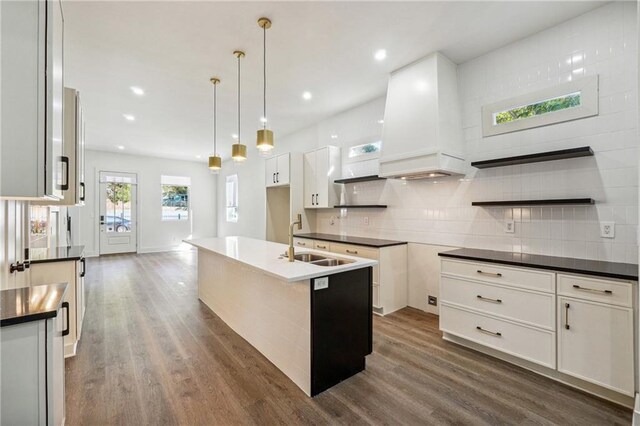 kitchen featuring decorative light fixtures, white cabinetry, sink, decorative backsplash, and a center island with sink