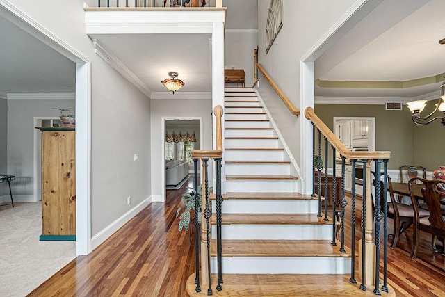 staircase featuring a chandelier, wood finished floors, visible vents, baseboards, and crown molding