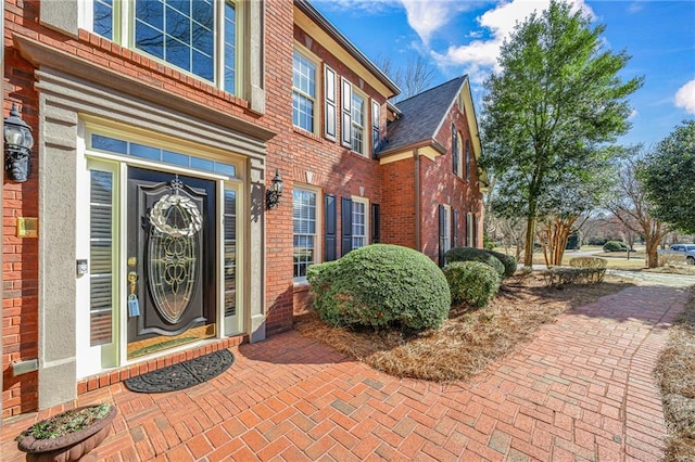 property entrance with a shingled roof and brick siding