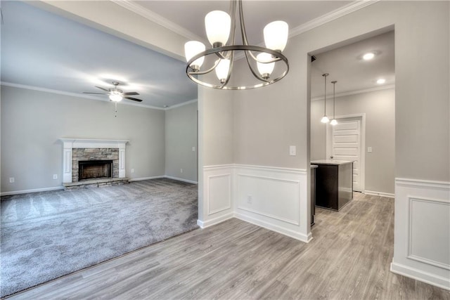 unfurnished living room with ceiling fan with notable chandelier, crown molding, light wood-type flooring, and a fireplace