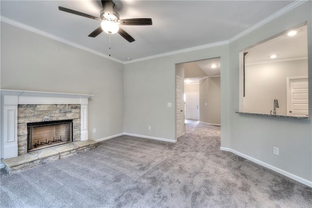 unfurnished living room featuring ceiling fan, sink, a stone fireplace, crown molding, and light carpet