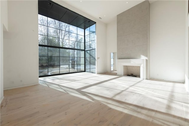 unfurnished living room with a fireplace, light wood-type flooring, a towering ceiling, and expansive windows