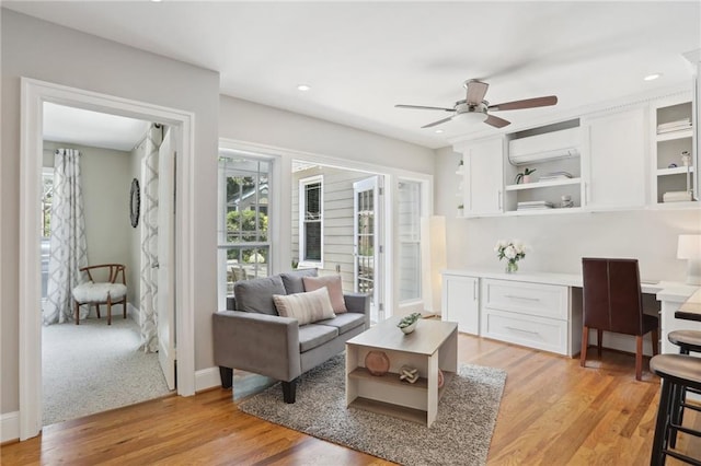 living room with ceiling fan, light wood-type flooring, built in desk, and a wall unit AC