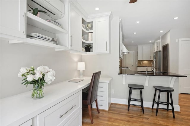 kitchen with white cabinetry, built in desk, stainless steel fridge, and a breakfast bar