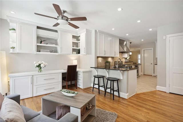 living room featuring a wall mounted AC, built in desk, ceiling fan, and light wood-type flooring