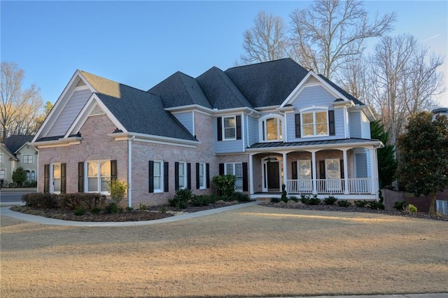 view of front facade featuring a porch, a front yard, brick siding, and a shingled roof