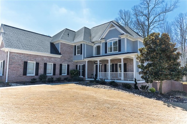 view of front of home with covered porch, brick siding, a front yard, and a shingled roof