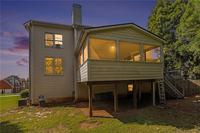 back house at dusk with a sunroom and central AC unit