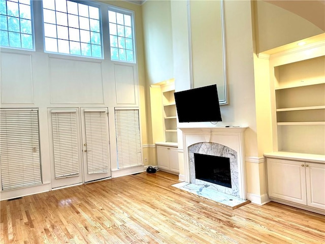 unfurnished living room with built in features, light hardwood / wood-style flooring, a high ceiling, and a premium fireplace