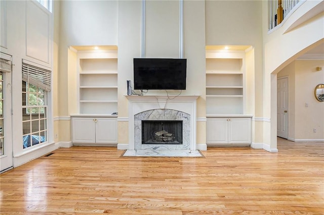 unfurnished living room featuring light hardwood / wood-style floors, a towering ceiling, a high end fireplace, and built in features