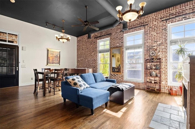 living room with rail lighting, brick wall, wood finished floors, and ceiling fan with notable chandelier