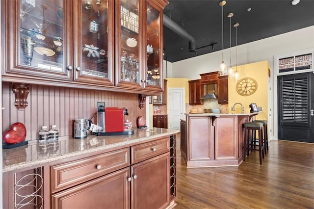 kitchen featuring tasteful backsplash, glass insert cabinets, a kitchen breakfast bar, dark wood-style flooring, and hanging light fixtures