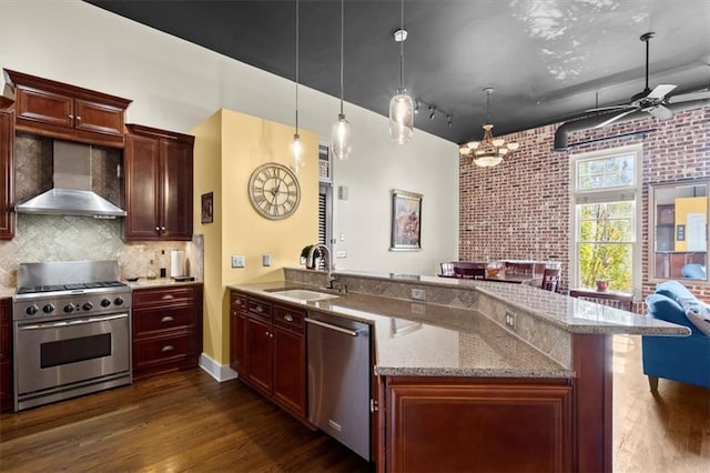 kitchen with dark wood finished floors, wall chimney exhaust hood, a peninsula, stainless steel appliances, and a sink