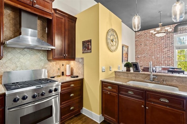 kitchen featuring stainless steel range, hanging light fixtures, a sink, wall chimney range hood, and backsplash