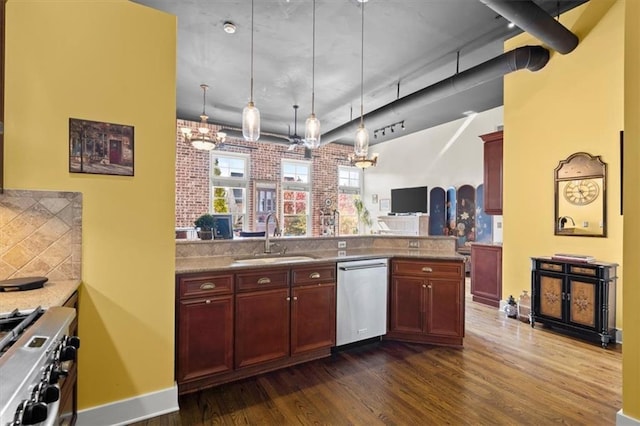 kitchen with dark wood finished floors, hanging light fixtures, a sink, stainless steel appliances, and backsplash