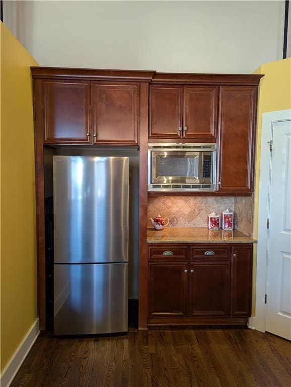 kitchen with light stone countertops, baseboards, appliances with stainless steel finishes, decorative backsplash, and dark wood finished floors