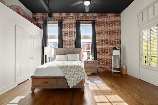 bedroom featuring baseboards, multiple windows, brick wall, and wood finished floors