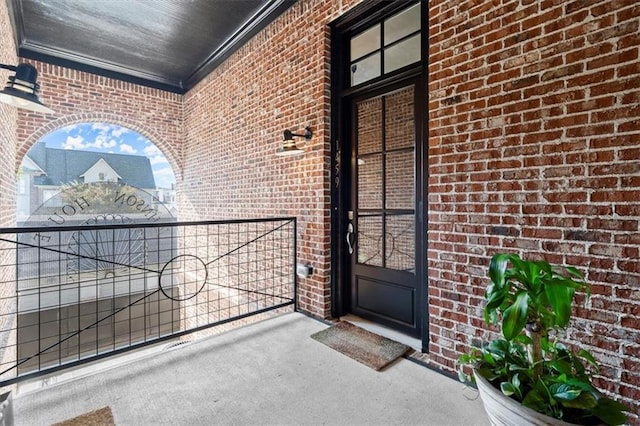 view of exterior entry featuring brick siding and a balcony