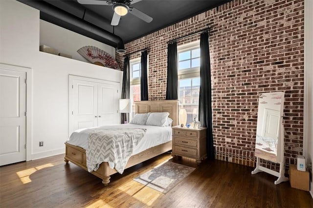 bedroom with ceiling fan, brick wall, baseboards, and dark wood finished floors