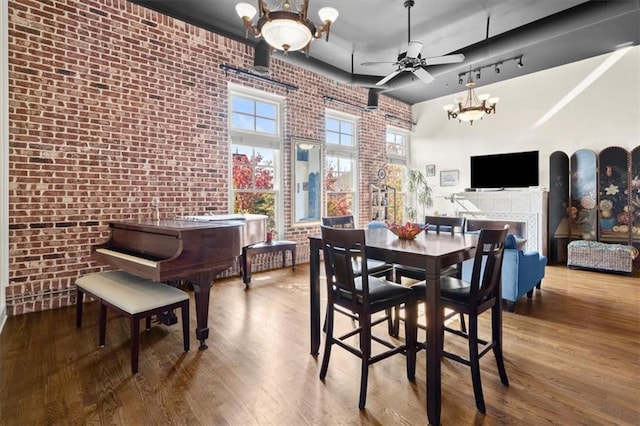 dining area featuring ceiling fan with notable chandelier, brick wall, a high ceiling, and wood finished floors