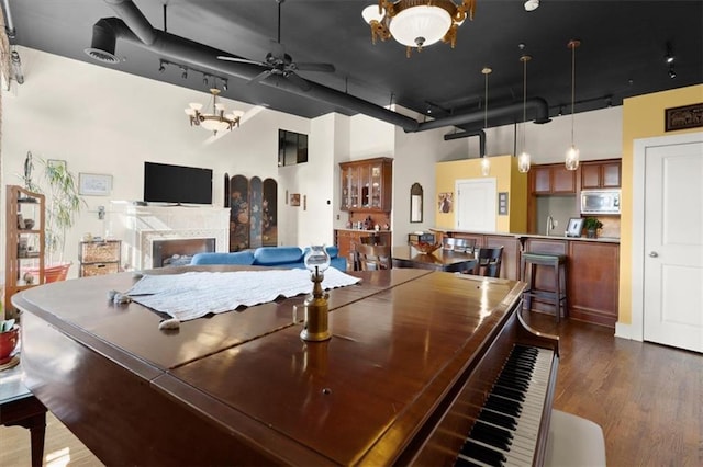 interior space featuring ceiling fan with notable chandelier, dark wood-style flooring, a fireplace, a towering ceiling, and visible vents