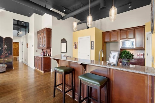 kitchen featuring stainless steel microwave, glass insert cabinets, dark wood finished floors, and a towering ceiling