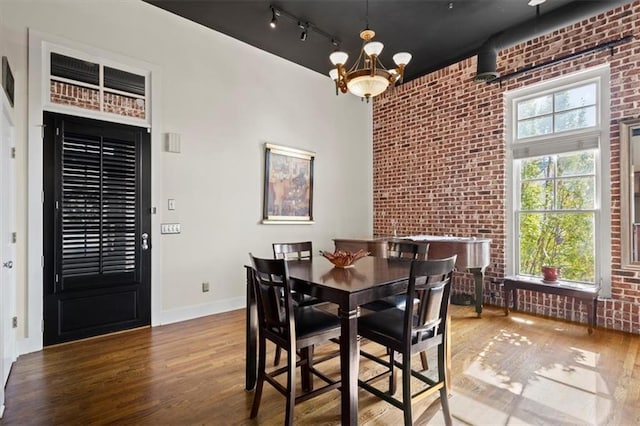 dining room with baseboards, brick wall, wood finished floors, and an inviting chandelier