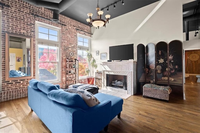 living room featuring an inviting chandelier, brick wall, a high ceiling, and wood finished floors