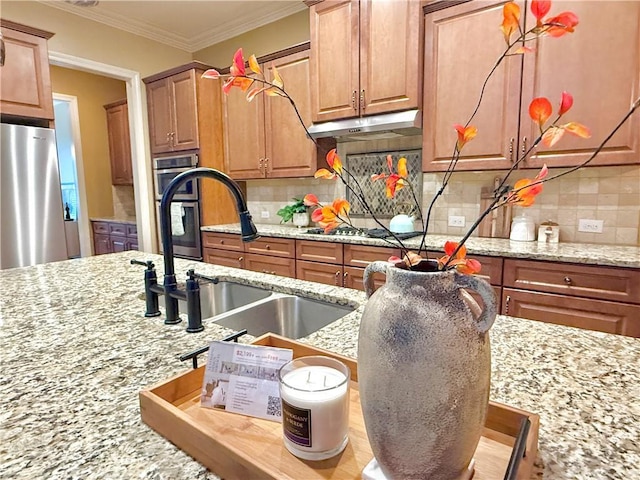 kitchen featuring backsplash, light stone countertops, a sink, freestanding refrigerator, and under cabinet range hood