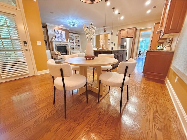 dining area featuring baseboards, ornamental molding, light wood-style flooring, and a fireplace