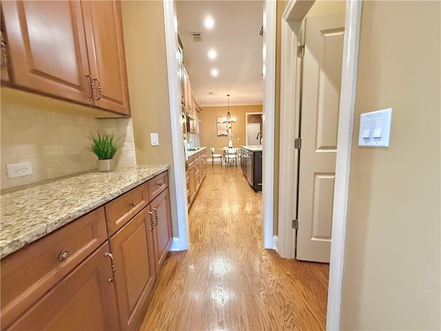 corridor featuring light wood-style floors, crown molding, and an inviting chandelier