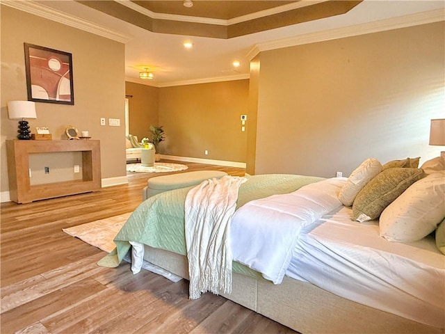 bedroom featuring a raised ceiling, recessed lighting, baseboards, wood finished floors, and ornamental molding