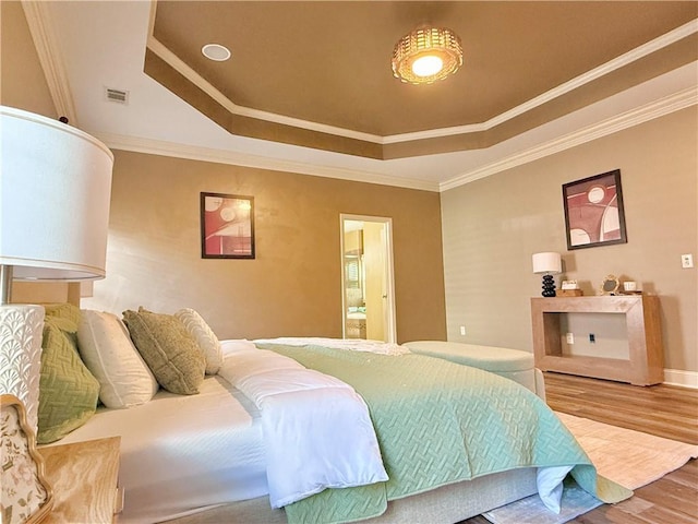 bedroom with ensuite bathroom, visible vents, wood finished floors, a raised ceiling, and ornamental molding