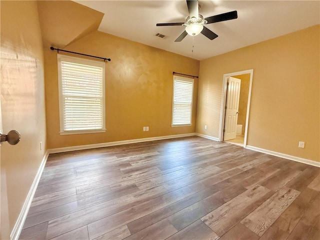 empty room with baseboards, a ceiling fan, hardwood / wood-style flooring, and visible vents
