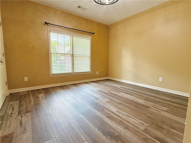 unfurnished room with baseboards, visible vents, and hardwood / wood-style flooring