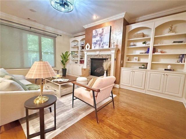 living room with crown molding, light wood-style flooring, built in features, and a stone fireplace
