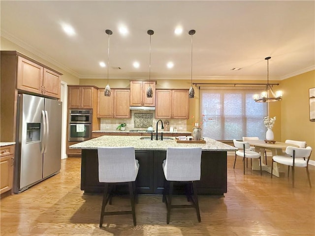 kitchen with decorative backsplash, light wood-style floors, a center island with sink, a sink, and stainless steel appliances